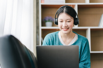Smart and positive Asian female freelancer or female college student sitting on sofa with laptop. Study from online webinars or home courses. Video calling and chatting