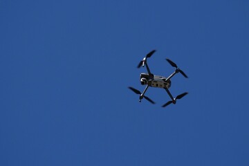 A drone flys overhead against a blue sky.