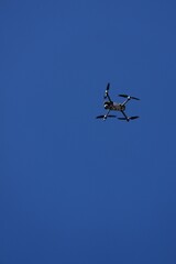 A drone flys overhead against a blue sky.