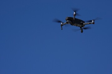 Fototapeta na wymiar A drone flys overhead against a blue sky.