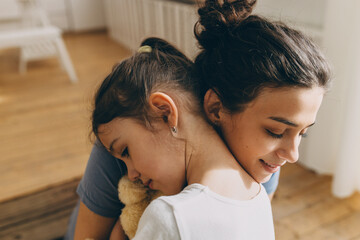 Close-up of young beautiful mother hugging with tenderness her sweet sad preschool daughter with...