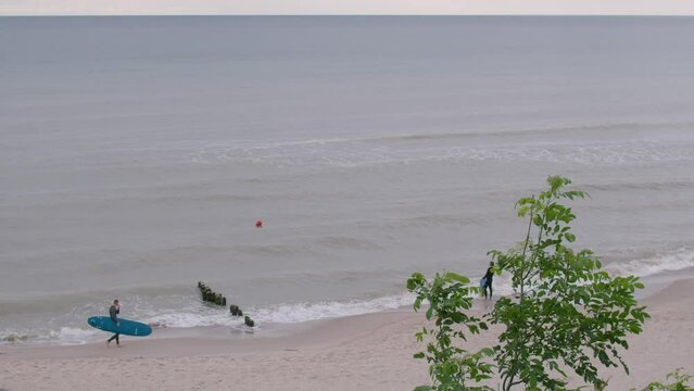 Top view of couple oy young male unrecognizable surfers in wetsuits walk on shore line before entering the water and surfing