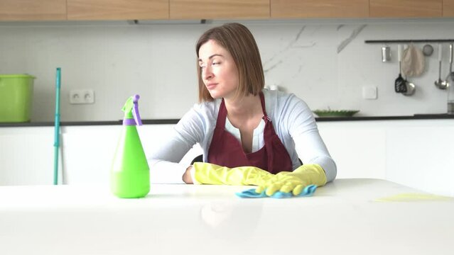 Tired attractive woman in yellow rubber gloves and red apron sits and wipes the table and feeling bad after exhausting cleaning day. Household concept