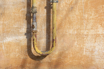 An old yellow U-shaped gas pipe against the background of a shabby plastered wall. There are...