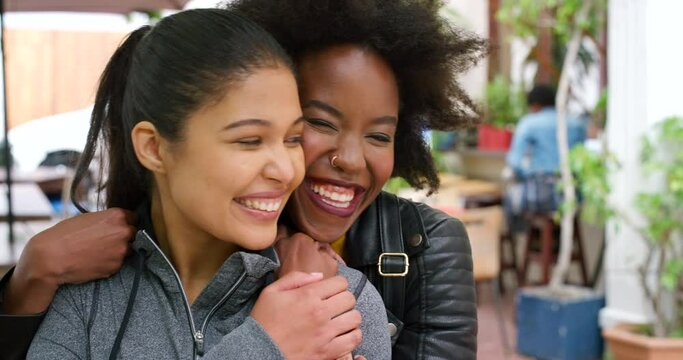 Two best friends bonding and hugging during a social visit. Happy female friends hugging outside in greeting. .Excited african girl embracing her smiling friend from behind in surprise meeting.