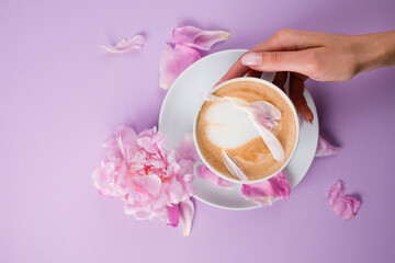 Female hands holding a cup of coffee. Blouse with romantic pink background and rose petals.
