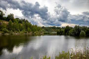 View of the lake on a cloudy day. Heavy clouds over the lake in summer. Reflection of the coast in the water on a summer day 
