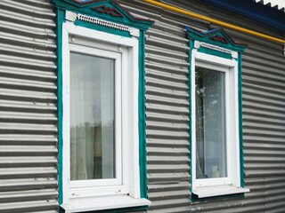 Two windows of rustic house with carved painted trim. Metal-line