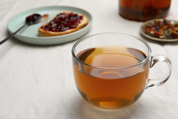 Cup of freshly brewed tea, dried herbs and bread with jam on white fabric