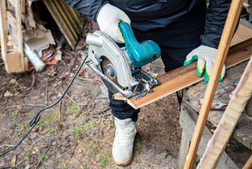 a carpenter sawing boards with a circular saw at their summer cottage