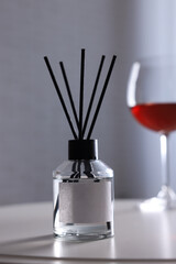 Reed diffuser and glass of wine on white table indoors