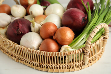 Wicker tray with fresh onions and garlic on white table, closeup