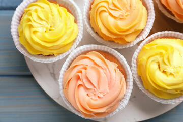 Stand with tasty cupcakes on light blue wooden table, top view