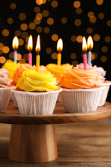 Stand with birthday cupcakes on wooden table against blurred lights, closeup