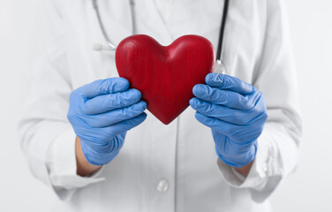 Doctor holding red heart on white background, closeup. Cardiology concept