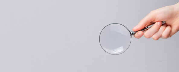 Magnifying lens in hand on gray banner with copy space for text.