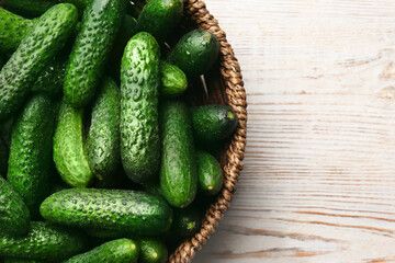 Fresh ripe cucumbers in wicker basket on white wooden table, top view. Space for text