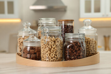 Glass containers with different breakfast cereals on white marble table in kitchen