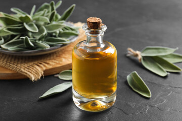 Bottle of essential sage oil and leaves on black table