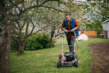 Portrait of a young farmer, gardener with a lawn mower on a plot of land in spring.