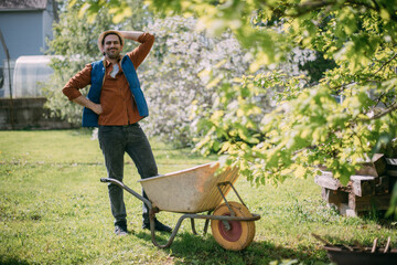 Portrait of a joyful farmer, a gardener with a garden cart on a plot of land in spring.