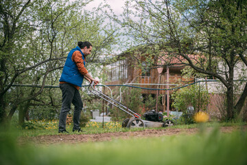 Portrait of a young farmer, gardener with a lawn mower on a plot of land in spring.