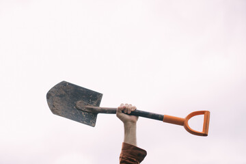 A man's hand holds a bayonet shovel on a white background. Metal shovel in his hands against the sky