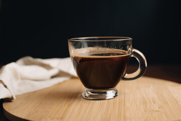 Taza de café, desayuno, taza de vidrio encima de bandeja de madera, en mesa de café de madera, con fondo oscuro, fondo negro, close-up