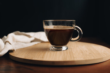 Taza de café, desayuno, taza de vidrio encima de bandeja de madera, en mesa de café de madera, con fondo oscuro, fondo negro, close-up
