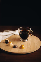 Obraz na płótnie Canvas Taza de café, taza de vidrio en mesa de madera, encima de bandeja de madera con bombones de chocolate, dulces de chocolate