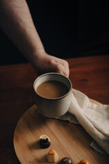 Mano sosteniendo taza de café, taza rústica, en mesa de madera oscura con bombones de chocolate