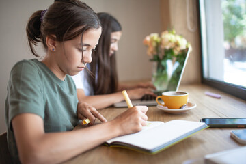 Obraz premium Two girls during the break, drinking coffee and eat, using modern devices, look at the laptop and talk