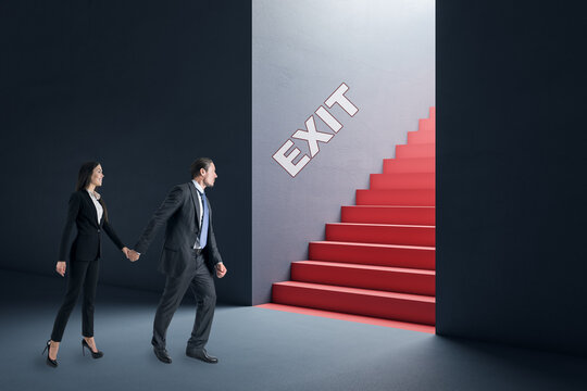 Thoughtful young businesswoman and man in concrete interior looking at red stairs exit. Way out, teamwork, solution and choice concept.