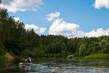 Fototapeta na wymiar Canoeing on Gauja river at cloudy day. Stormy sky. Pines on shore. Two people in boat.