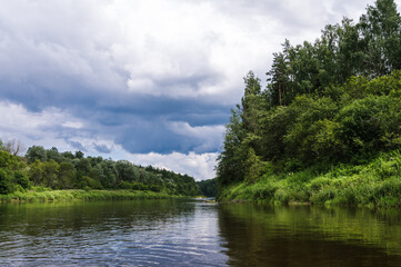 Scenic landscape of river Gauja at cloudy day. Stormy sky. Summer nature. Green trees. Reflection in water.