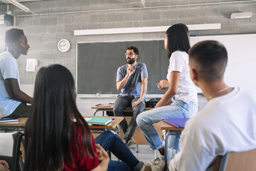 Teenager students listening and talking to friendly young male teacher - Group discussion in High...