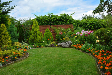 zielony trawnik w ogrodzie otoczony krzewami ozodbnymi i kolorowymi kwiatami