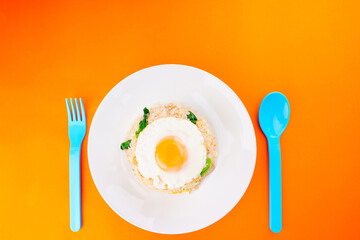 Thai food delicious homemade Fried rice with pork and kale Above is a fried egg on a white plate and a blue fork spoon on an orange paper background. Leave a blank space above for the text.