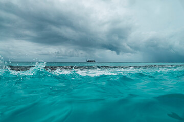 Traditional Maldivian Dhoni Boat passes by on the turquoise blue sea horizon on a stormy day - Medium 