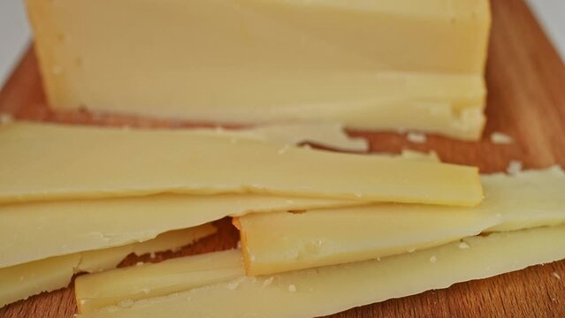 Sliced pieces of delicious hard cheese on wooden board close-up. Fresh tasty cheese, dairy food, cooking ingredient. European edam gouda parmesan goat cheese