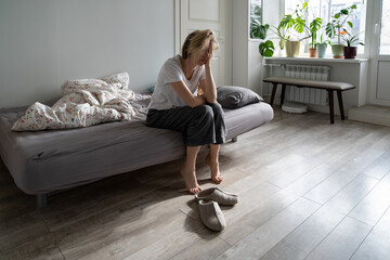 Upset depressed woman holding head in hands sitting on bed at home, unhappy frustrated single female suffering from depression or grief, feeling lonely, thinking about problems. Depressive disorder