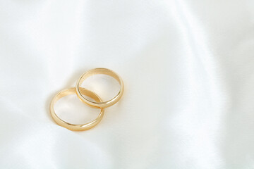 Two gold wedding rings on a white satin.