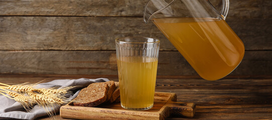 Woman pouring fresh kvass from jug into glass on wooden background