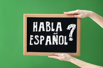 Hands holding chalkboard with text HABLA ESPANOL? (DO YOU SPEAK SPANISH?) on green background