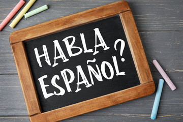 Chalkboard with text HABLA ESPANOL? (DO YOU SPEAK SPANISH?) on wooden background