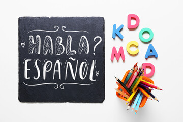 Board with text HABLA ESPANOL? (DO YOU SPEAK SPANISH?), letters and pencils on white background