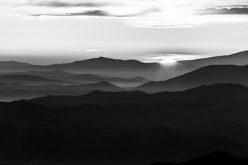 Distant sunset above layers of mountains and valleys with mist and fog - 517554027