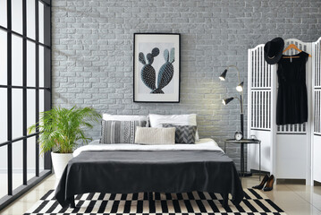 Interior of stylish bedroom with poster, glowing lamp and folding screen