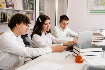 Obraz premium Chemistry lesson in labaratory. Education online in class with group of pupils studying on laptop, smiling and having fun together.