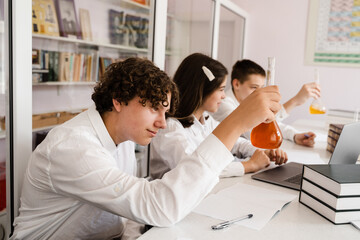 Pupil holding flask with liquid for experiments in laboratory. Education concept. Group of pupils studying chemistry lesson in school.